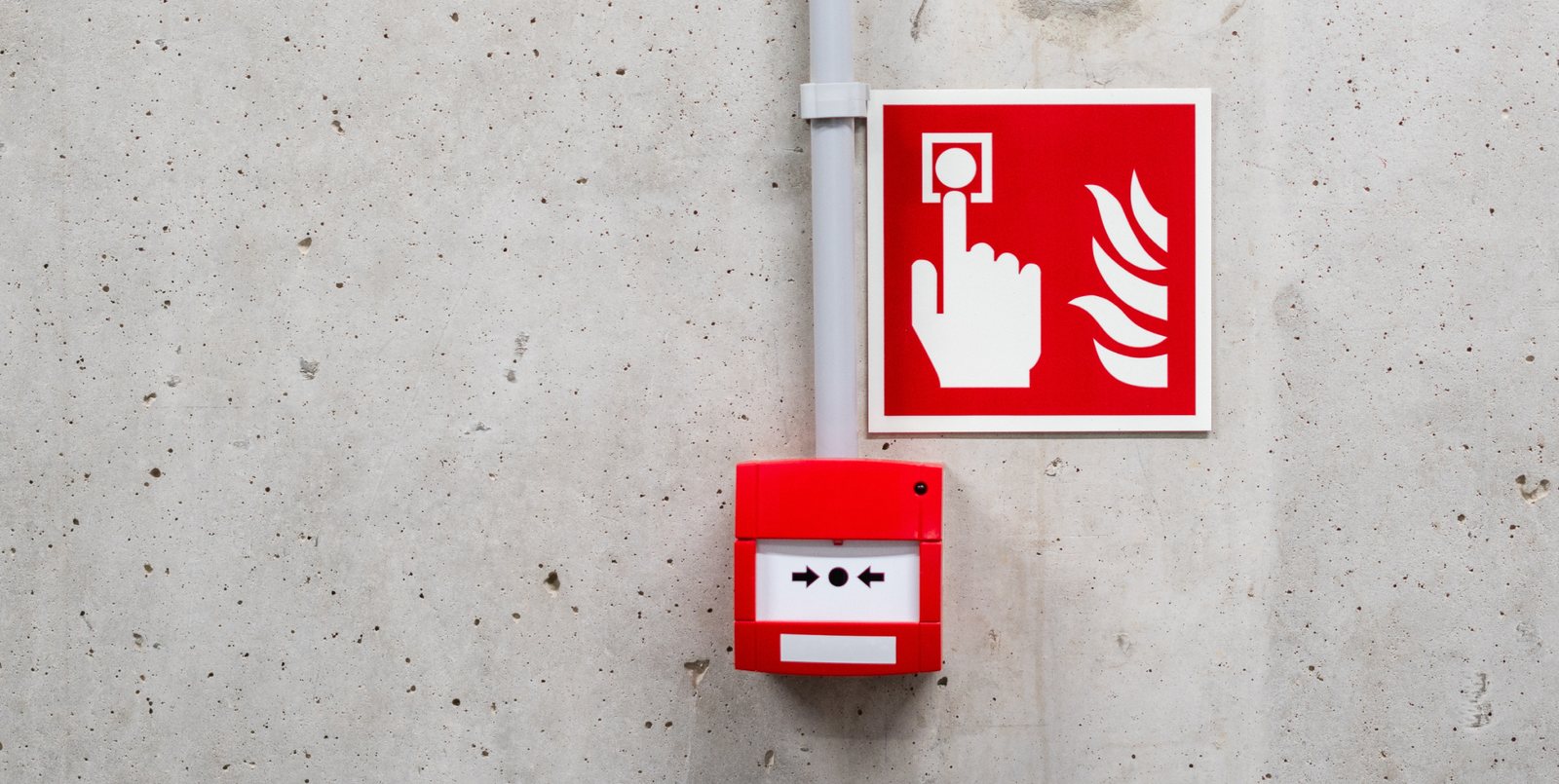 Roter Handfeuermelder mit Hinweisschild an einer Betonwand